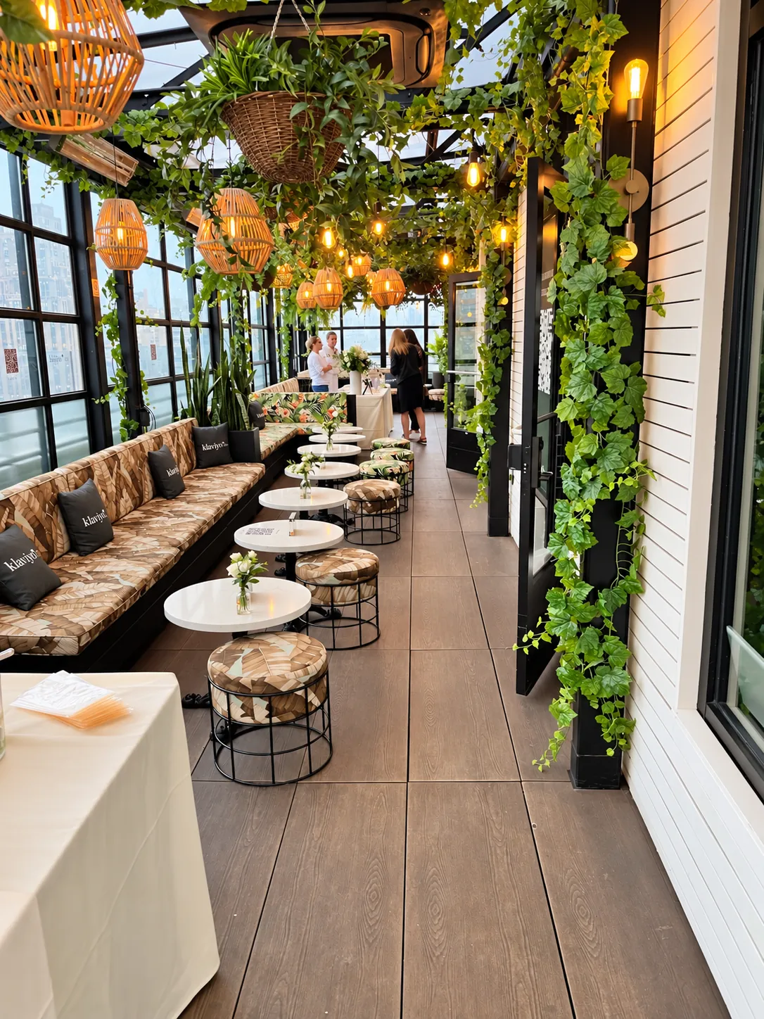 A plant-filled glass terrace set with banquettes, small tables and hanging lanterns as guests arrive